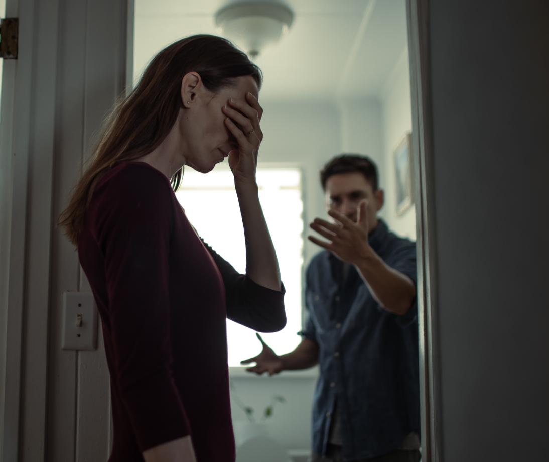Person covering face, another gesturing behind them.